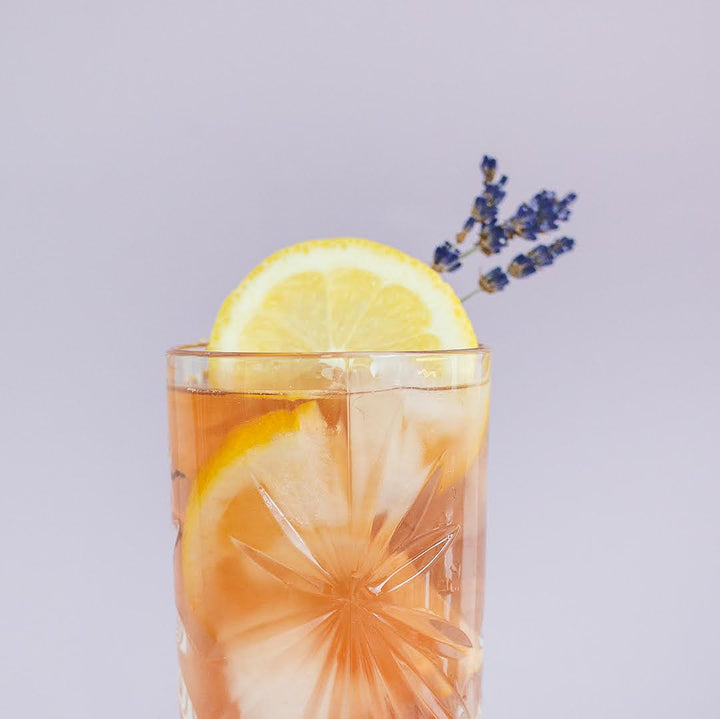 A glass of lavender earl grey tea with a slice of lemon and a sprig of lavender garnish, on a light background.
