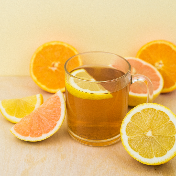 A clear glass mug filled with lemon tea on a table, surrounded by slices of lemon and orange.