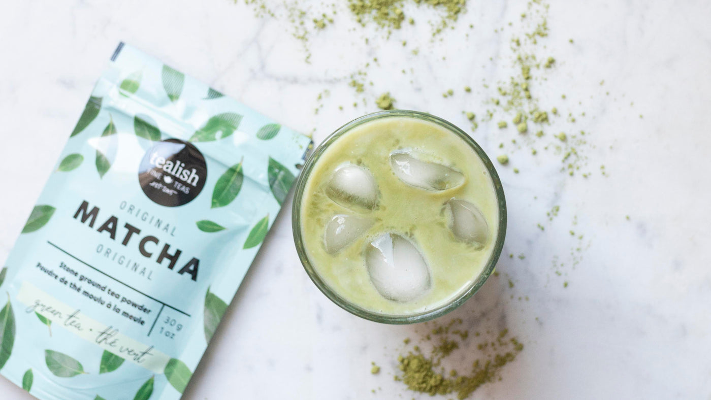 Matcha green tea powder packet with a glass of matcha latte on a white background
