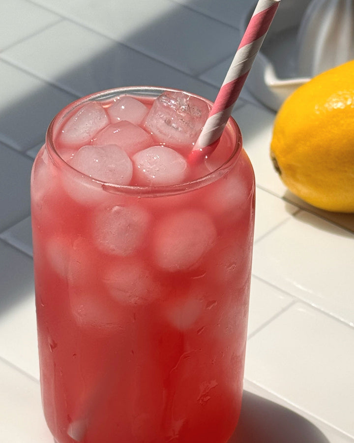 Glass of pink lemonade with ice and a straw on a white surface