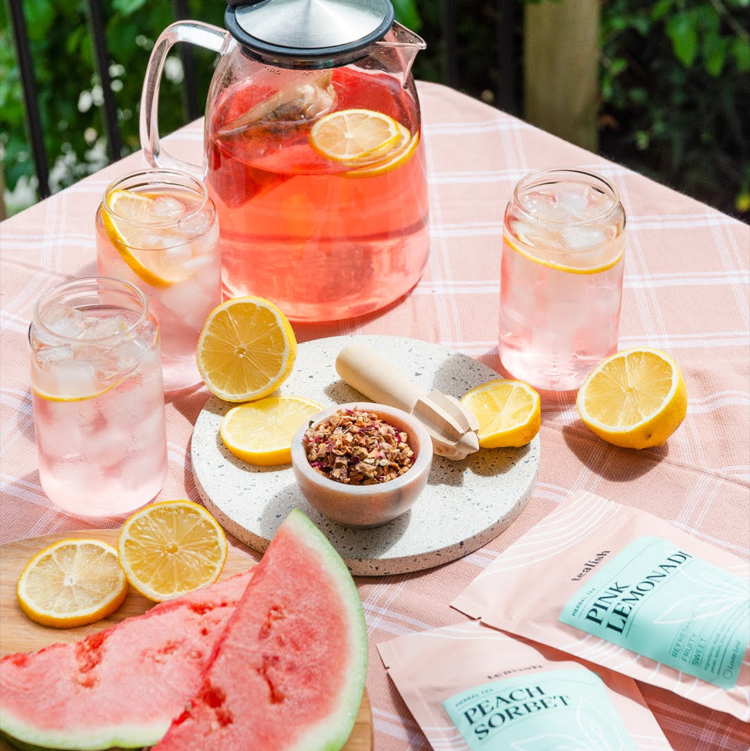 Outdoor setting with pink lemonade, watermelon, and lemon slices on a tablecloth.