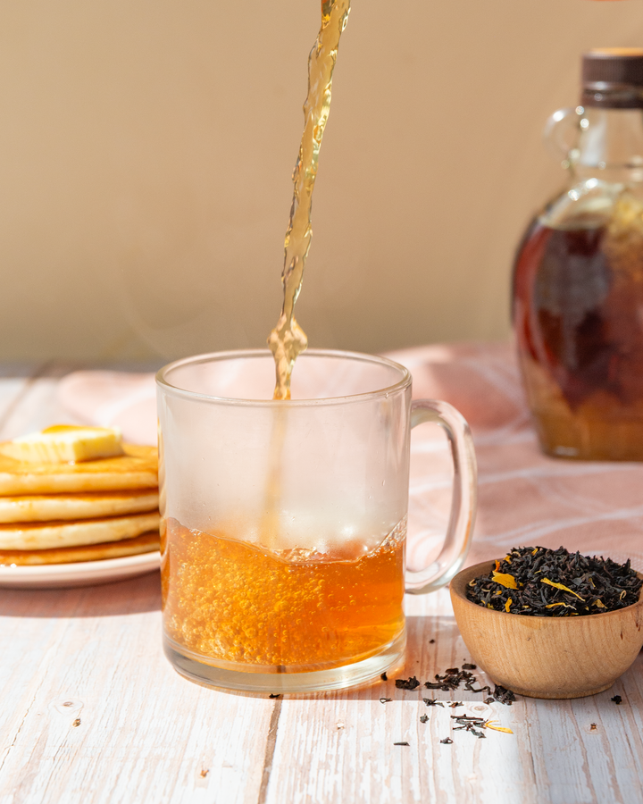 A picture of tea pouring inside a cup with breakfast items on the side