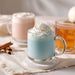 Glass mug with blue drink and whipped cream, surrounded by pumpkins and cinnamon sticks on a neutral background